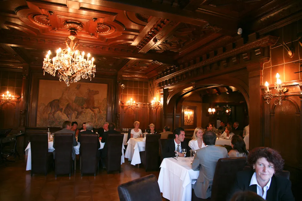 Saal mit Kassettendecke, Kronleuchter und Gästen an gedeckten Tischen